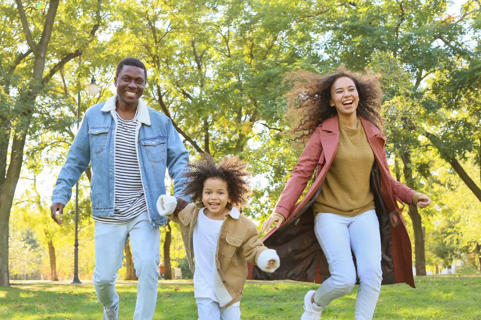 Pai, mãe e filha correndo de mãos dadas num parque