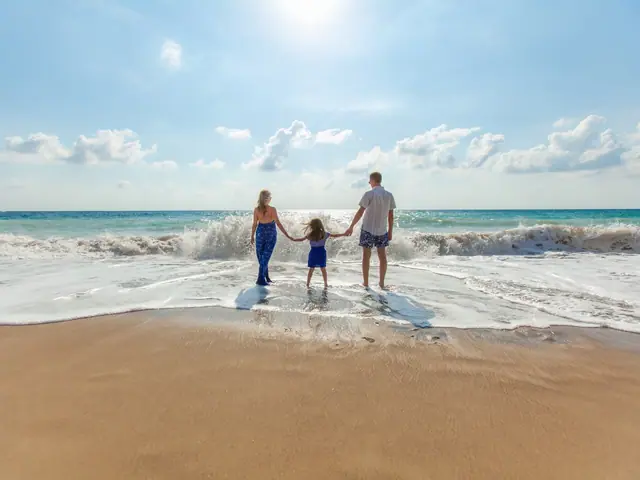 Pai, mãe e filha de mãos dadas na beira do mar